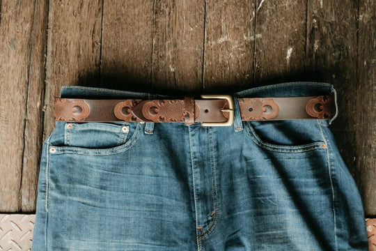 Blue jeans with a brown leather belt on a wooden surface