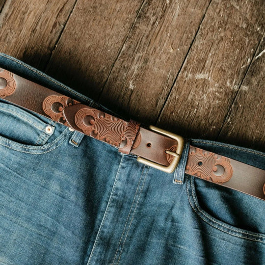 Close-up of blue jeans with a brown leather belt on a wooden surface