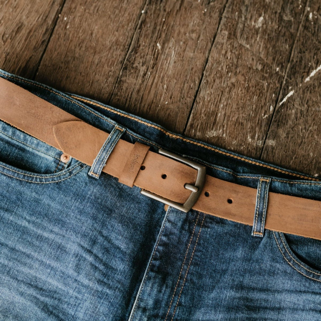 Brown leather belt on blue jeans against a wooden background