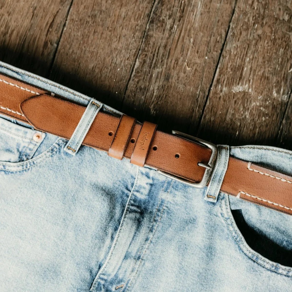 Close-up of blue jeans with a brown leather belt on a wooden surface