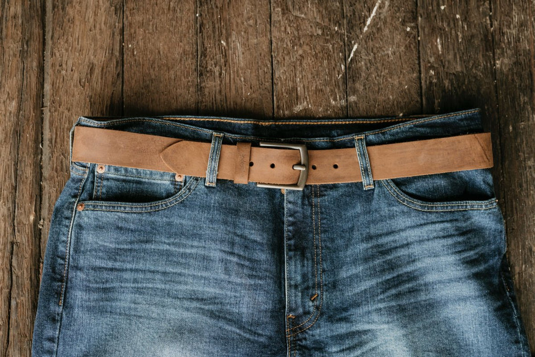 Blue jeans with a brown leather belt on a wooden surface