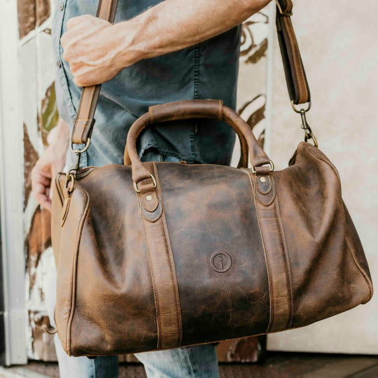 Brown leather duffel bag held by a person with a blurred background