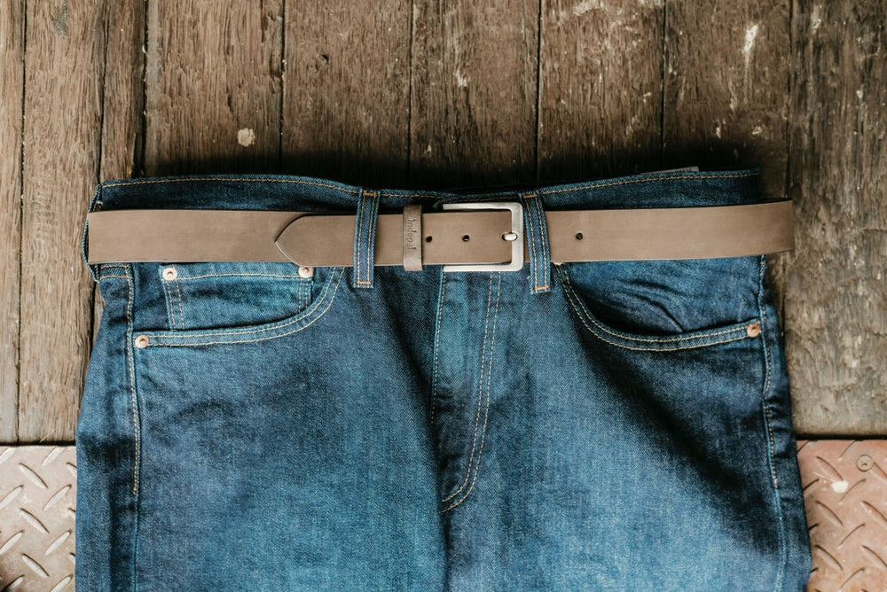 Blue jeans with a brown leather belt on a wooden floor