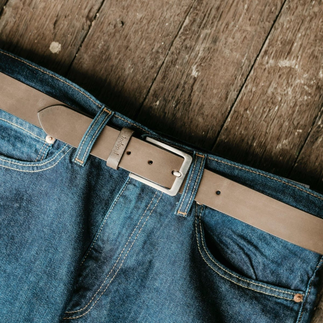 Blue jeans with a brown leather belt on a wooden surface