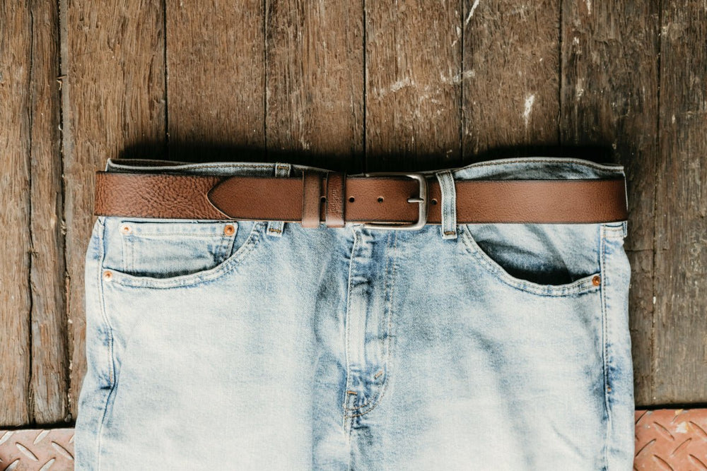 Blue jeans with a brown leather belt on a wooden surface