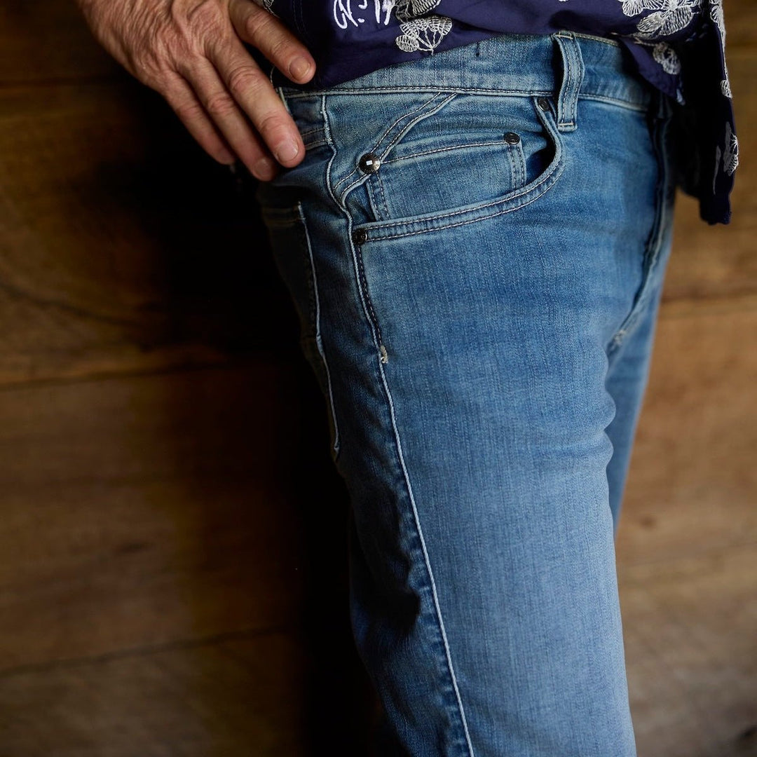 Person wearing a floral-patterned shirt and blue jeans on a wooden floor.