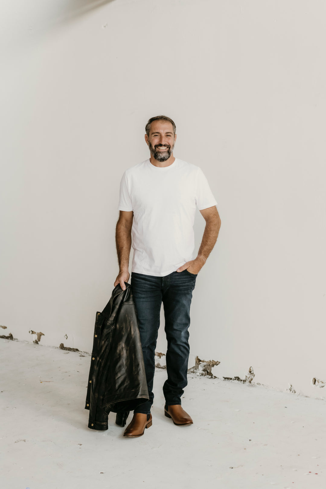 Man holding the Hailwood Distressed Brown Leather Jacket by Indepal Leather from Bolt + Buckle, styled with a white t-shirt, dark jeans, and brown boots.