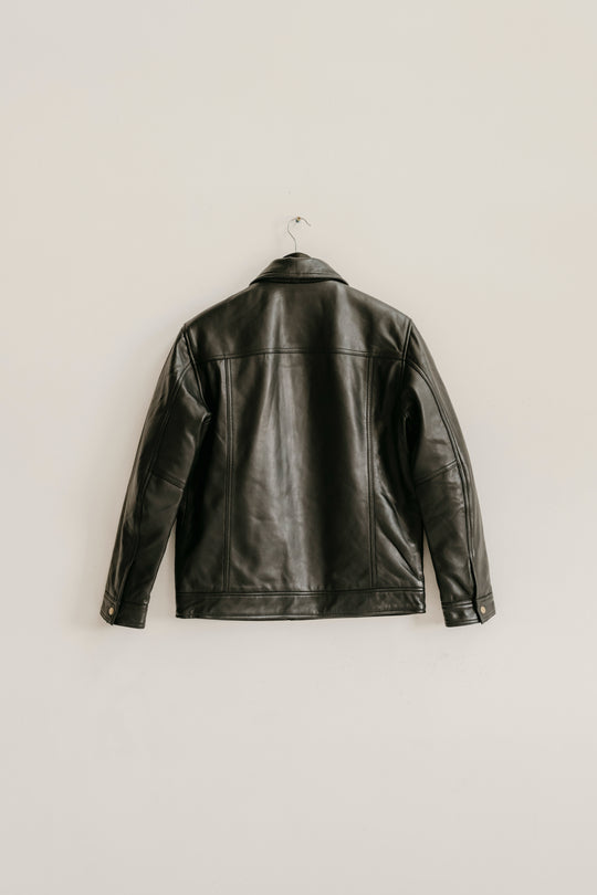 Back view of the Hallwood Black Leather Jacket by Bolt + Buckle hanging on a white wall.