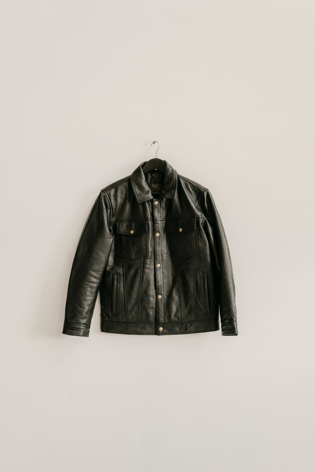 Hallwood Black Leather Jacket by Bolt + Buckle hanging on a white wall.