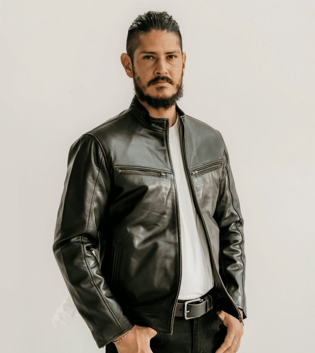 Man wearing the Ollie Black Leather Jacket by Indepal Leather from Bolt + Buckle, styled with a white t-shirt and black pants, standing against a white wall.