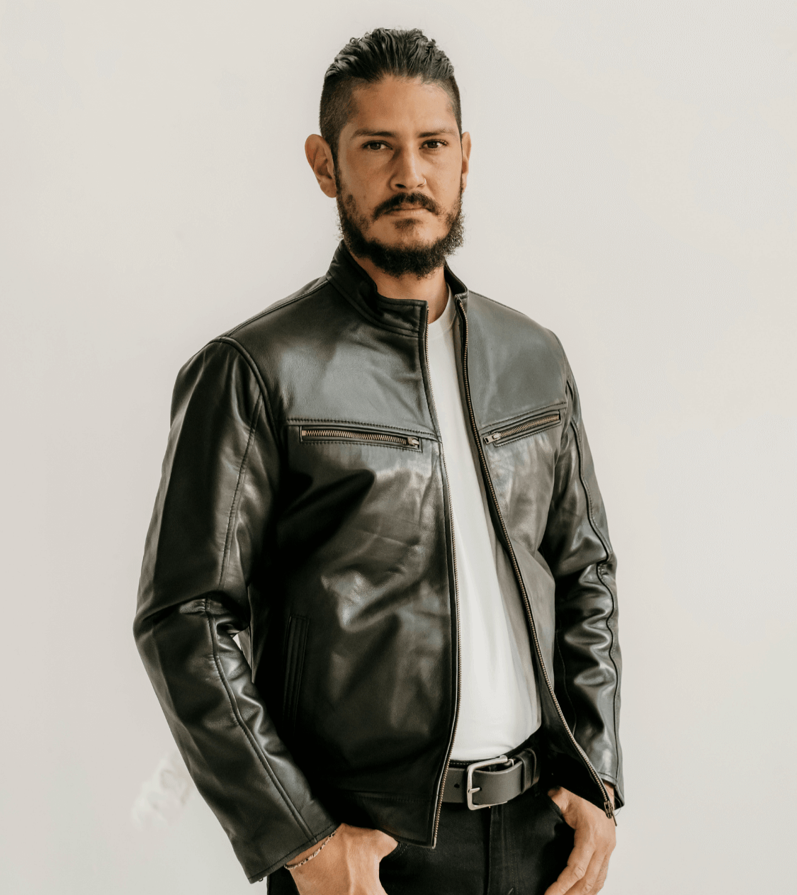 Man wearing the Ollie Black Leather Jacket by Indepal Leather from Bolt + Buckle, styled with a white t-shirt and black pants, standing against a white wall.
