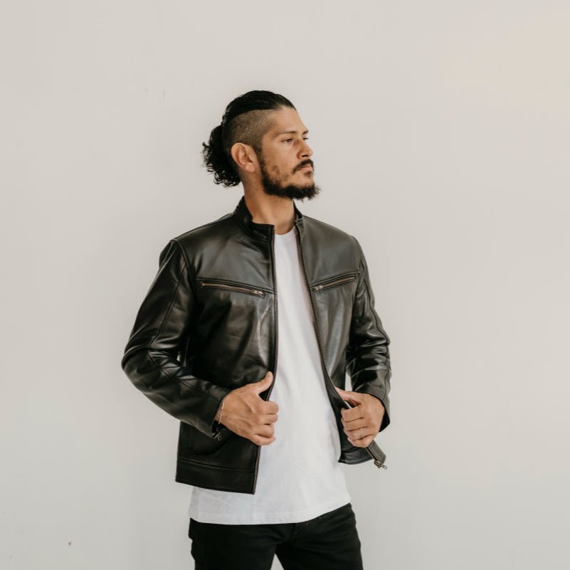Man wearing the Ollie Black Leather Jacket by Indepal Leather from Bolt + Buckle, styled with a white t-shirt and black jeans, looking to the side against a white wall.